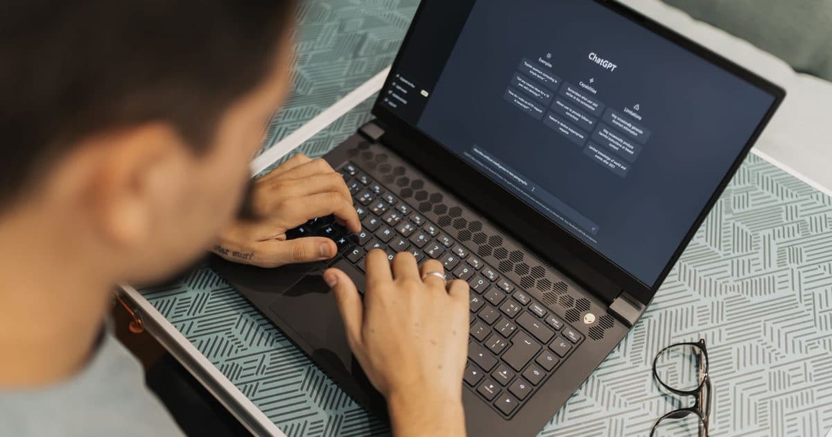 Person asking an AI chat assistant a question on a laptop, glasses beside the keyboard