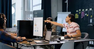 Enterprise team collaborating around computers with dashboards on screen.