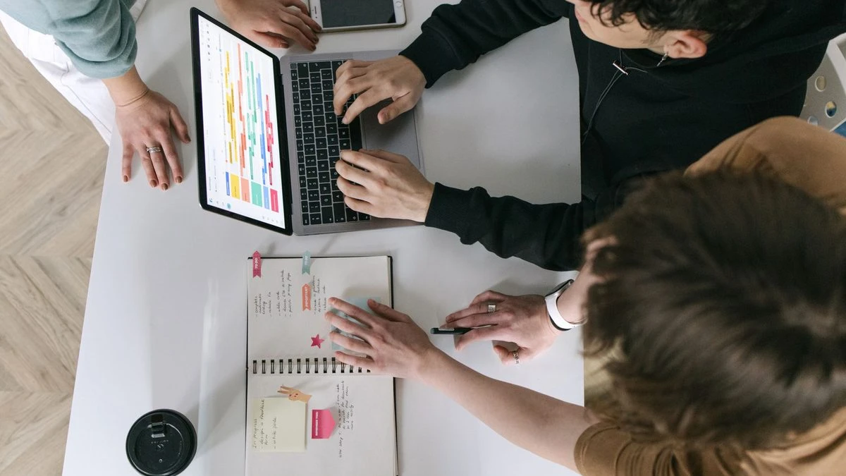 A high-angle view of a team collaborating over a laptop and notebook in a modern office.