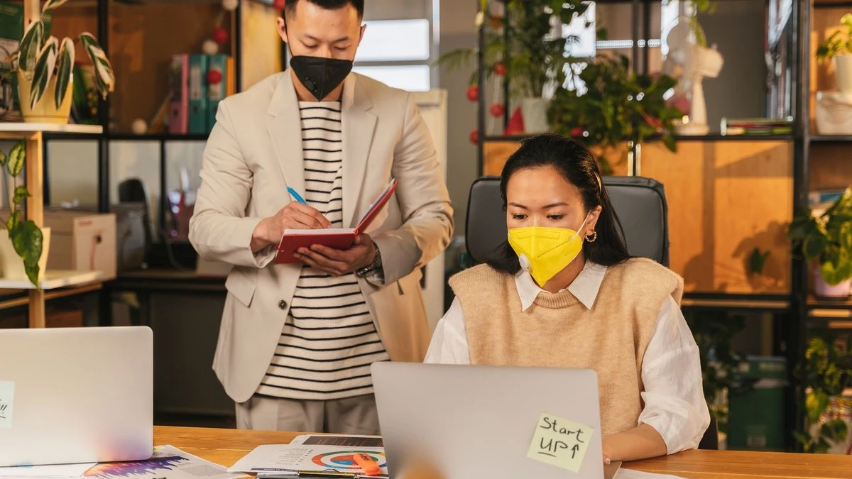 Colleagues in masks working together in a plant-filled modern office setting.