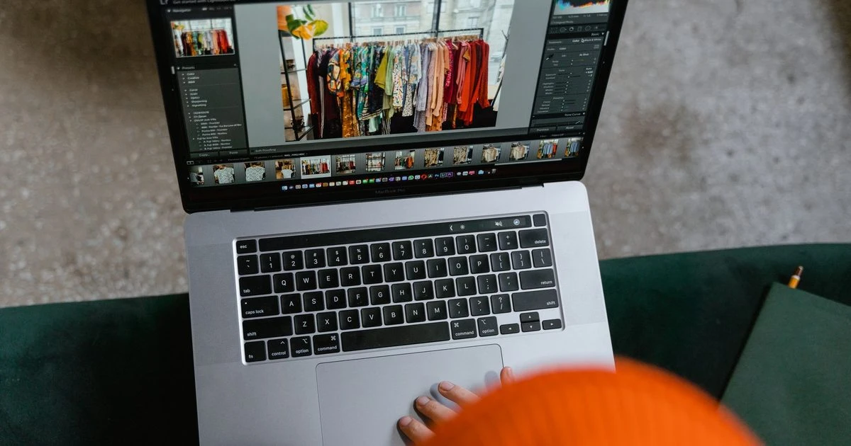 Pessoa editando fotos de produtos de uma loja de roupas em um laptop.