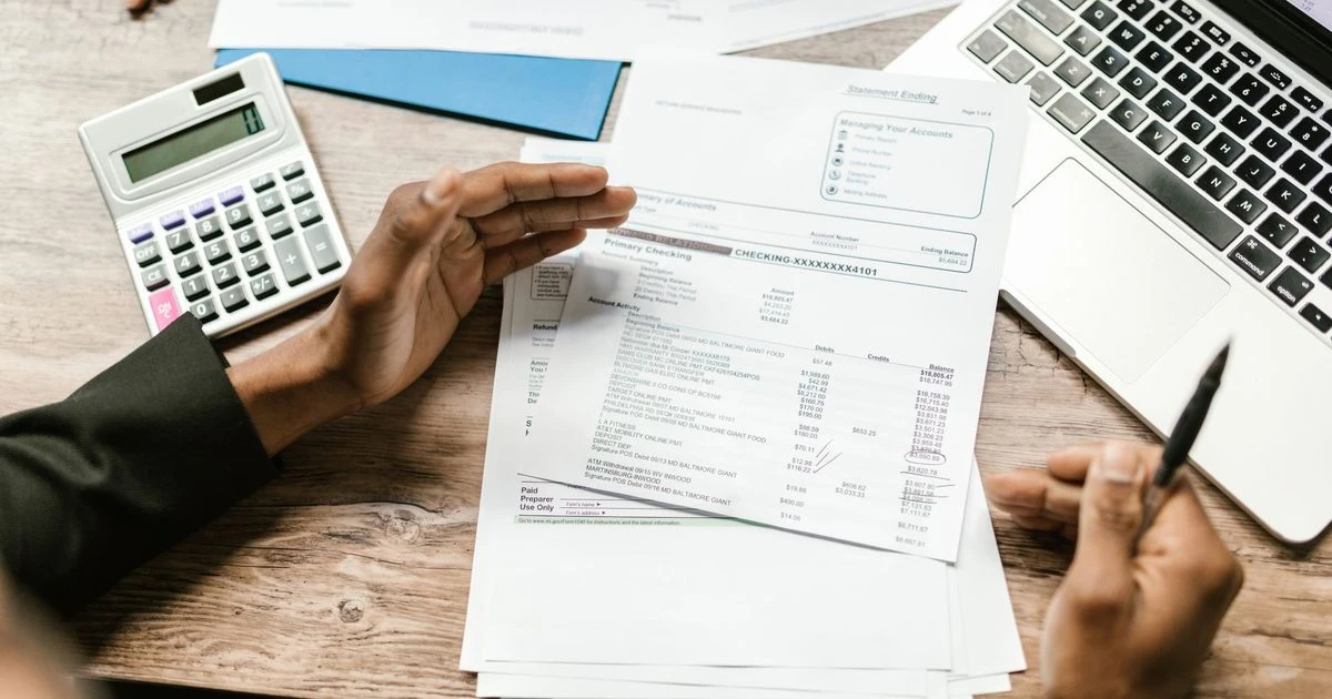 Finance professional reviewing printed financial reports beside a laptop and calculator.