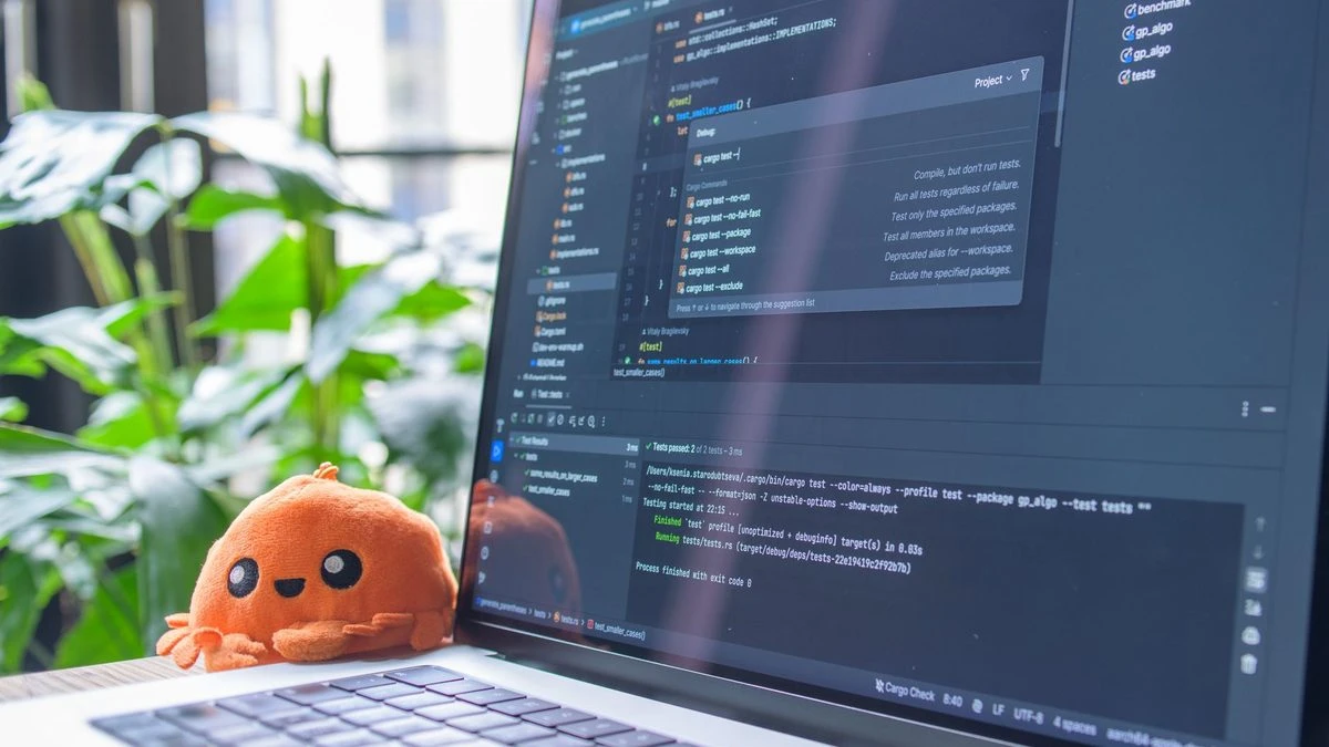 Open laptop with code editor displaying, next to an orange plush toy and green plants.