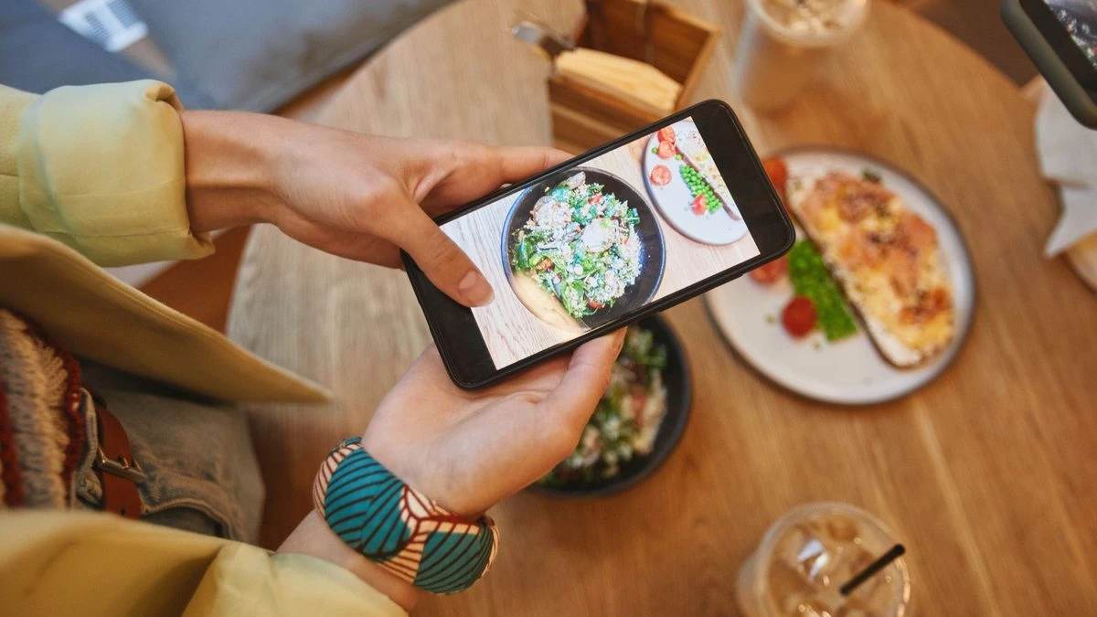 Person taking a photo of delicious meals on a smartphone in a cozy cafe setting.