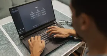 Person testing an AI assistant on a laptop, hands on the keyboard with glasses beside the computer
