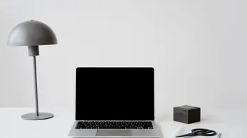A minimalist office setup featuring a closed laptop, modern lamp, and a notepad with scissors on a white background.