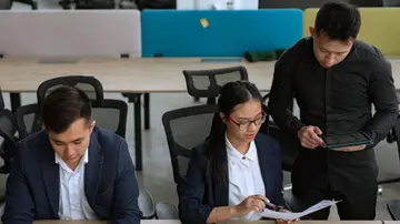 A professional team collaborating in a modern office setting, focusing on documents and technology.