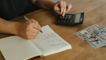 Pessoa revisando um orçamento pessoal com calculadora e registros anonimizados.