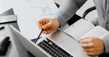 Profissional documentando um piloto de IA no trabalho, revisando laptop e anotações no escritório.
