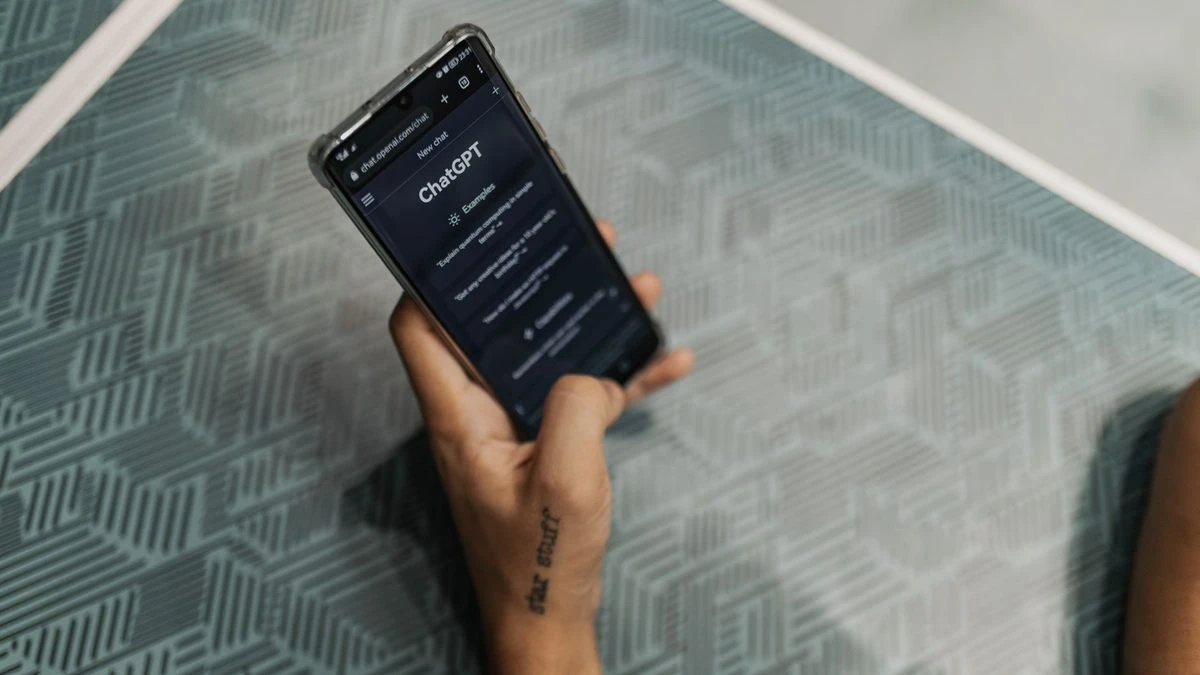 Close-up of a person holding a smartphone displaying the ChatGPT application interface on a patterned table.
