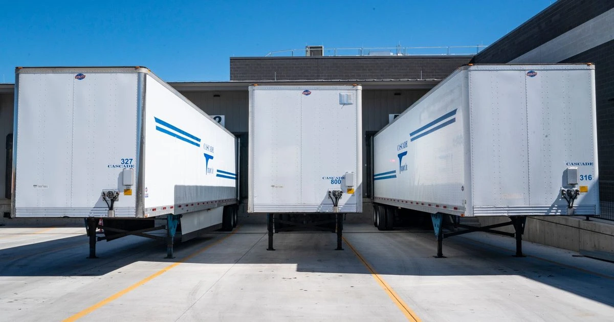 White freight trailers parked at loading docks under a clear sky.