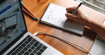 Learner comparing online course platforms using written criteria in a notebook beside a laptop.