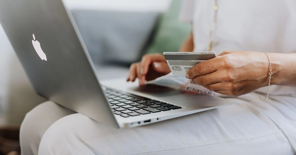 Online shopper holding a credit card while completing a purchase on a laptop.