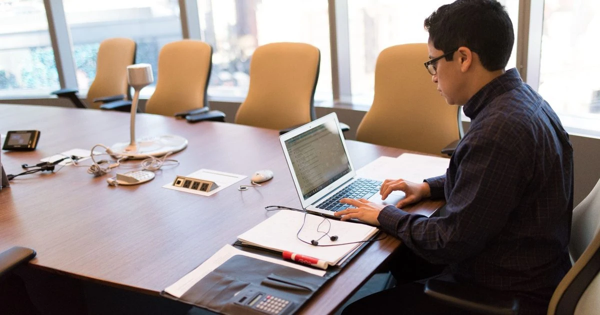 Professional working on a laptop at a conference table in a modern office.