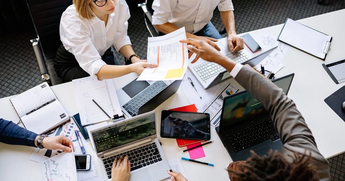 Startup founders collaborating around a table with laptops, documents and a tablet.