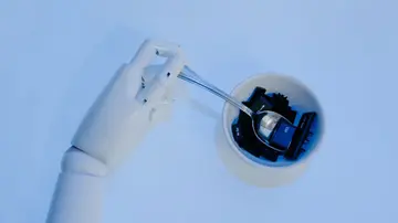 A robotic hand holds a spoon filled with keyboard keys, symbolizing AI and technology fusion.
