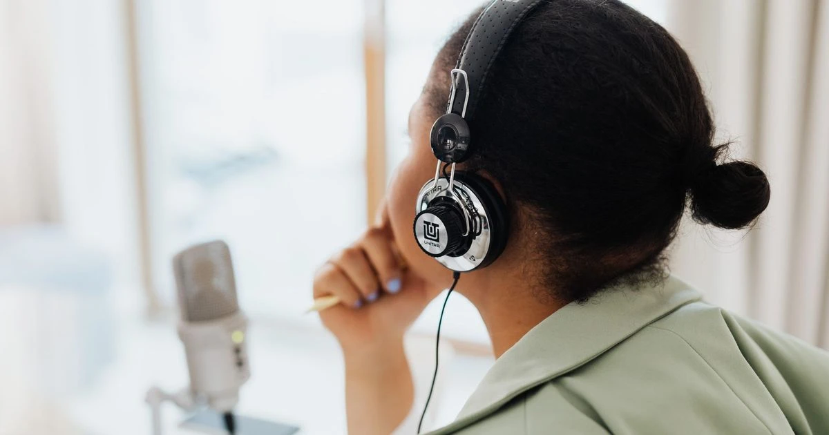 Woman wearing headphones speaking into a podcast microphone by a window